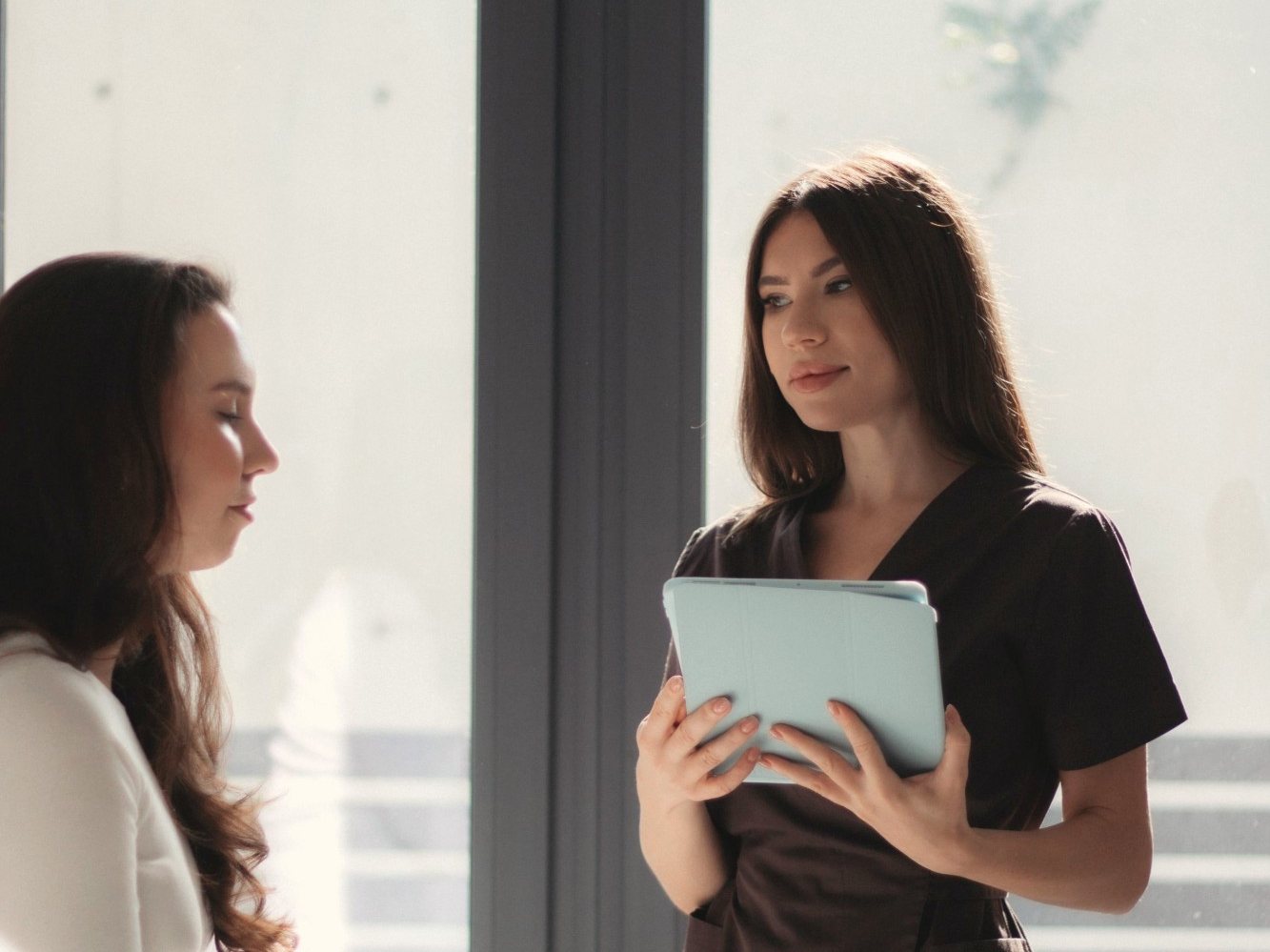 A clinician with a tablet talking with a patient by a sunlit window