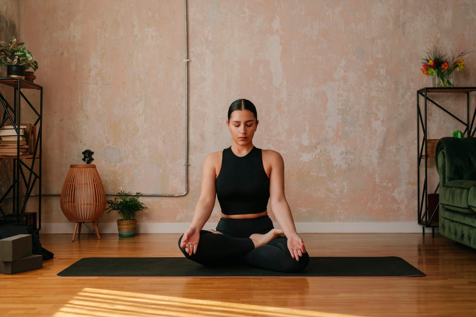A woman meditating on a yoga mat in a sunlit room